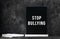 Black chalkboard white text Stop Bullying on dark background with notebook and pen. School education board with sign