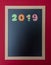 Black chalkboard with wooden frame, number 2019 in colorful numbers, red wall background, copy space