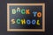 Black chalkboard with wooden frame, text back to school in colorful letters, black wall background