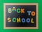 Black chalkboard with wooden frame, text back to school in colorful letters, green wall background