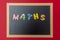 Black chalkboard with wooden frame, word, text maths in colorful letters, red wall background