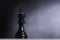 Black chess king standing under ray beam over dark foggy background with negative copy space, business strategy