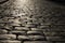 Black cobbled stone road background with reflection of light seen on the road. Black or dark grey stone pavement texture.