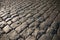 Black cobbled stone road background with reflection of light seen on the road. Black or dark grey stone pavement texture.