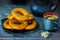 Black coffee cup with bagels on a black bowl and three pieces of sugar on a blue background