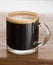 Black coffee and froth in glass mug wood table