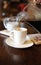 Black coffee is poured into a cup from glass serving jug. Devices for manual coffee brewing in the background