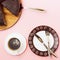 Black coffee, tableware and chocolate cake on a pink background