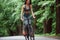 On black colored bike. Female cyclist on asphalt road in the forest at daytime