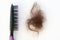 Black comb and a bundle of brown hair on a white background.