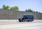 Black compact cargo mini van running on the road with concrete protection wall on the side