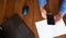 Black computer on old wooden desk. Mobile phone in man`s with blue shirt hand.