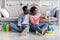 Black couple with cleaning tools sitting on floor, using smartphone