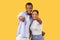 Black couple pointing at camera, friendly and inviting, yellow background