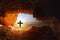 Black cross with bright light in front of dark cave in the dry hostile desert with boulders