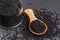 Black cumin seeds in a wooden spoon and glass jar over black background. Ayurvedic medicinal herb nigella sativa. Kalonji for
