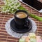 Black Cup of coffee with milk on a saucer, marshmallows, a bouquet of lilies of the valley and a smartphone