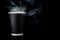 Black cup of coffee with a white cap on a black background. Hot drink with steam