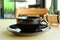 Black cup on wooden table with blurry coffee shop in background