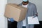 Black delivery man wearing mask and gloves, holding cardboard box and clipboard