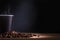 Black disposable cup of coffee with smoke and scattered coffee beans on dark background