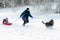 Black dog leading mother with daughter sledging through deep snow in a rural setting