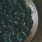 Black dried raisins in plate over wooden background, square crop