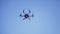 Black drone flying against the blue sky with spinning blades, bottom view. Clip. Compact quadcopter controlled by