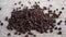 Black dry peppercorn falling on a textured rough gray jute mat