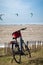 Black Electric bike with a red basket parked in grass against seaside with many kitesurfers