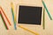 Black, empty, blank chalkboard with colored pencils on brown wooden desk flat lay from above