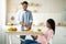 Black expectant lady reading book while her boyfriend cooking balanced breakfast in kitchen