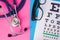 Black eyeglasses with eye test chart for measure visual acuity and medical stethoscope in two colors background: blue and pink. Co