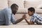 Black father competing in arm-wrestling with his little son at home