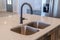 Black faucet and stainless steel double basin sink on kitchen island of home