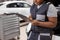 black female Auto Mechanic Making Car Checkup, in Uniform Writing and holding Clipboard