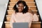 Black Female Using Laptop Gesturing Thumbs-Up Sitting On Steps Indoor