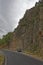 A Black Fiat Car parked in the layby of a Small Spanish Mountain Road, with two cyclists riding up the gentle hill.