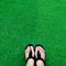 Black flip flops on green lush artificial grass, summer and vacations concept