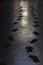 Black footprints from shoes on a sidewalk in a dark evening light.