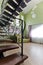 Black, forged staircase in a high, green interior