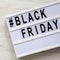 `Black friday` words on a lightbox on a white wooden surface, top view. Close-up