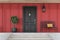 Black front door of red house with tree and bench