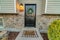 Black front door with wreath of house with stone wall and gray exterior siding