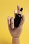 Black frosted glass bottle with a pipette in a wooden hand on an isolated yellow background.