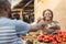 black girl selling tomatoes in a local african market to a male customer smiling and feeling happy and satisfied