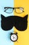 Black glasses, alarm clock and sleep mask on blue and yellow background composition