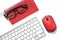 Black glasses on a red notebook, red mouse and white keyboard isolated on a white