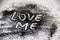A black glitter on the white background. A words love me painted on the black sand