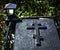 Black granite tombstone with an Orthodox cross on a grave at night in a cemetery with a luminous old lamp